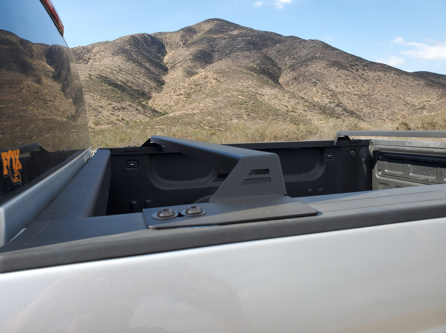View of a bed rack for a 2014-2018 Silverado/Sierra 1500 mounted on a truck, made by Range Industries, showcasing its sleek design against a mountainous backdrop.