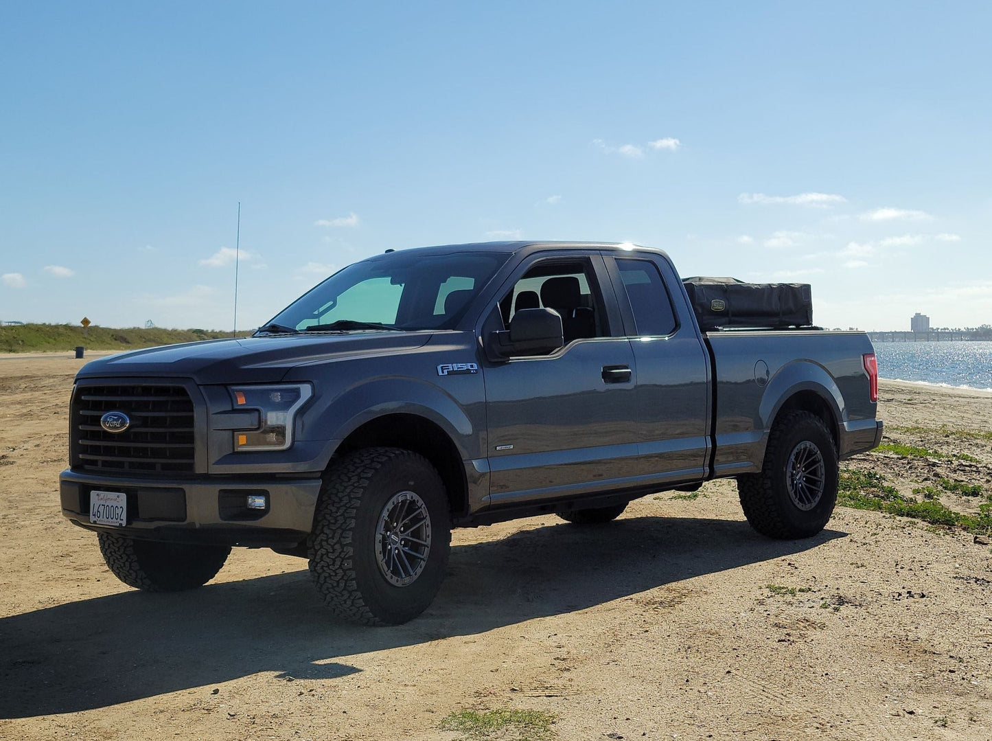 2015+ F-150 Low Profile Rooftop Tent Rack Kit by Range Industries, showing a gray F-150 parked on a sandy beach with the ocean in the background.