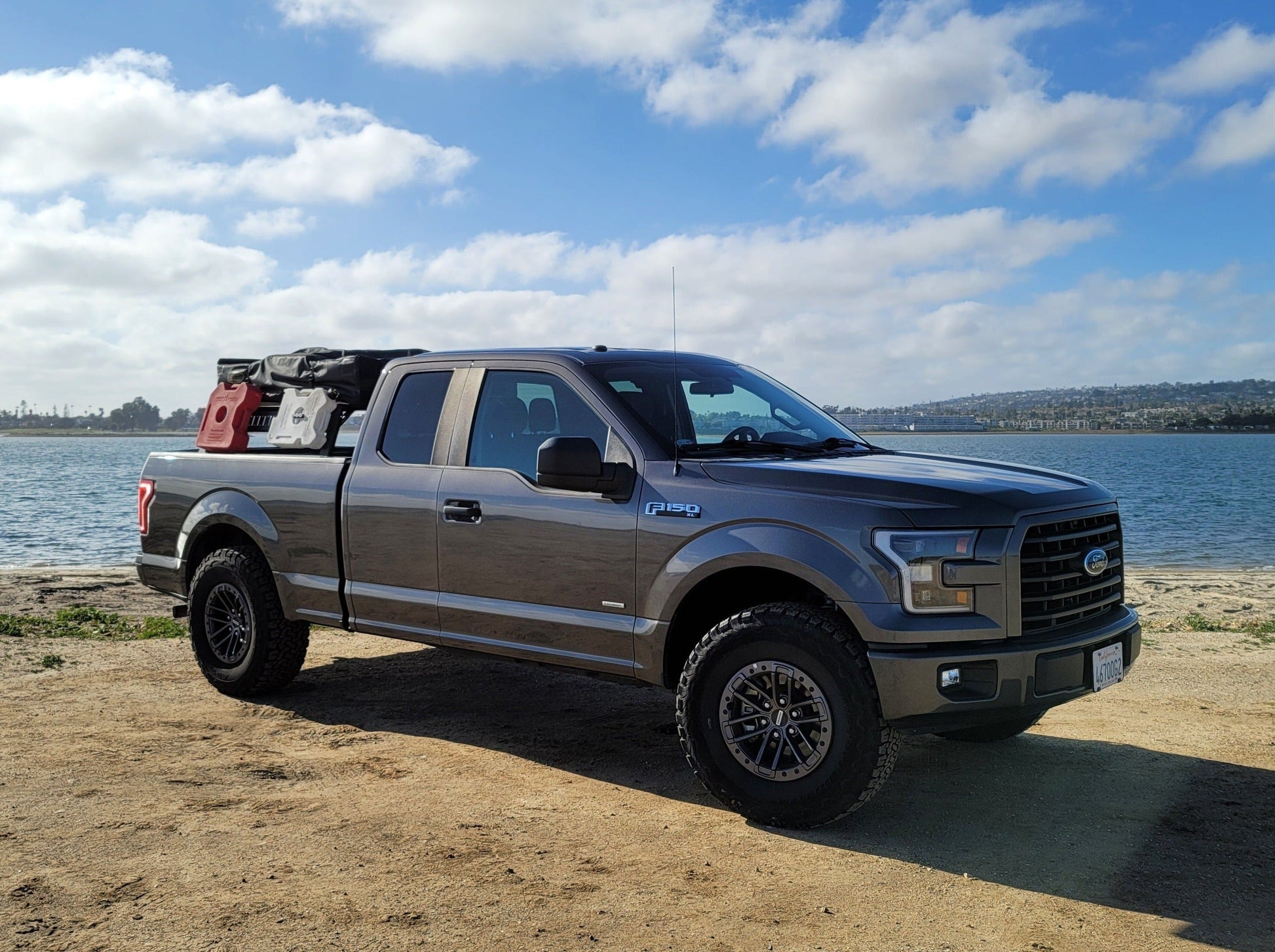 2015+ F-150 Mid Height Rooftop Tent Rack Kit installed on a Range Industries Ford F-150, showcasing the truck parked by the water with gear in the truck bed.