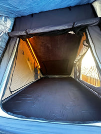 Interior view of the RTT Insulation in a Telurika Rooftop Tent by Dirtbox Overland, showcasing a cozy sleeping area with soft lighting and a comfortable, black floor surface.