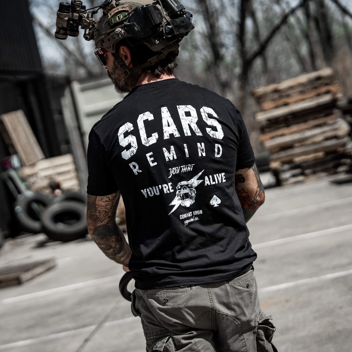 Man in tactical gear with a black t-shirt showing 'Scars Remind You That You're Alive' by Combat Iron Apparel.
