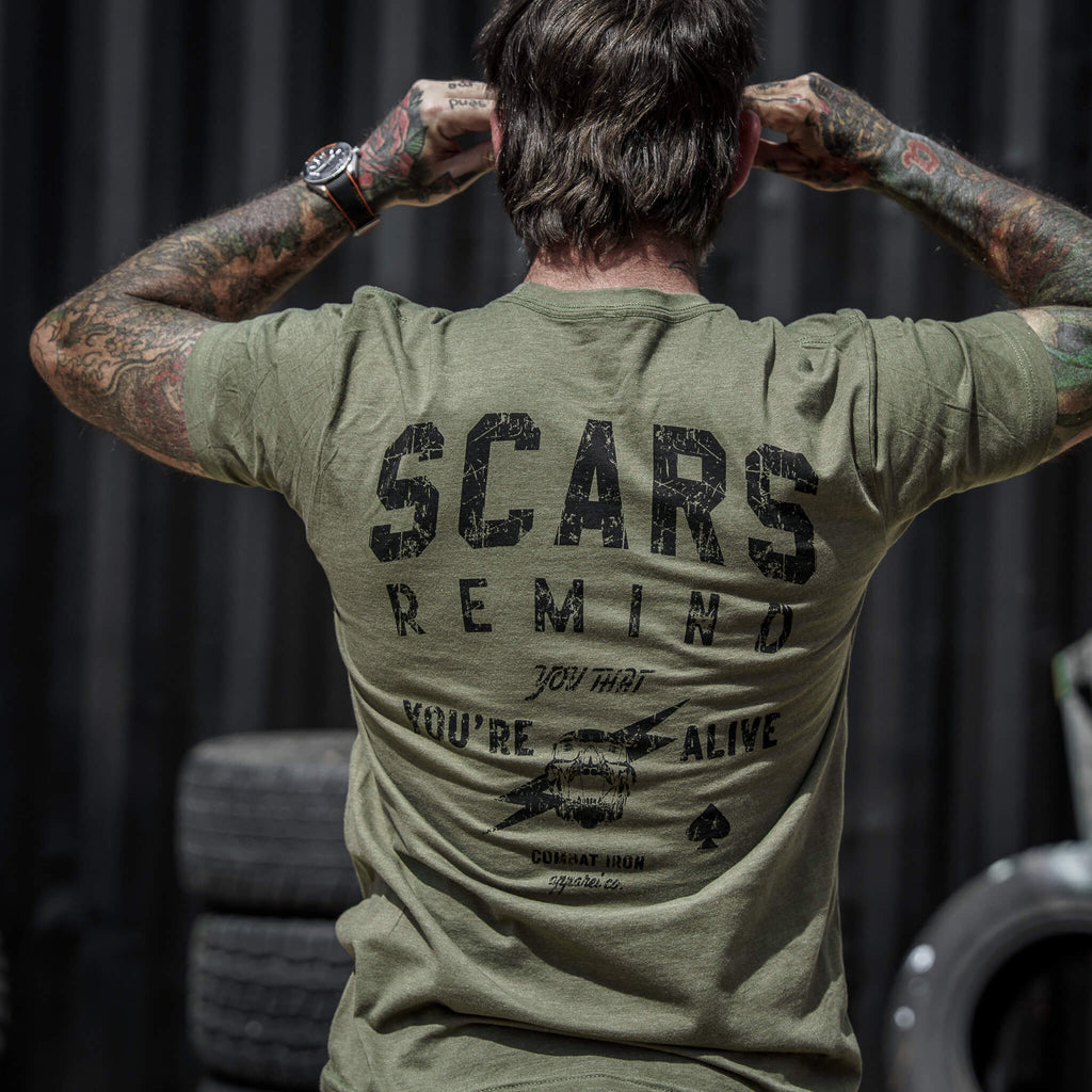 Back view of an olive green t-shirt featuring the text 'Scars Remind You That You're Alive' by Combat Iron Apparel.