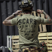 Load image into Gallery viewer, Close-up of a tattooed man holding gear while in an olive green t-shirt with 'Scars Remind You That You're Alive' by Combat Iron Apparel.