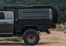 Load image into Gallery viewer, Close-up of the Dirtbox Overland Flatbed System Camper Box on a pickup truck, highlighting its durable exterior and ample storage for outdoor adventures.