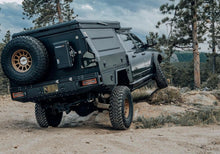 Load image into Gallery viewer, Rear view of the Dirtbox Overland Flatbed System Camper Box on a truck, demonstrating its adaptability for both work and leisure activities in the wilderness.