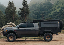 Load image into Gallery viewer, Dirtbox Overland Flatbed System Camper Box mounted on a rugged truck, showcasing the versatile and customizable design ideal for adventures or work, set against a natural backdrop.