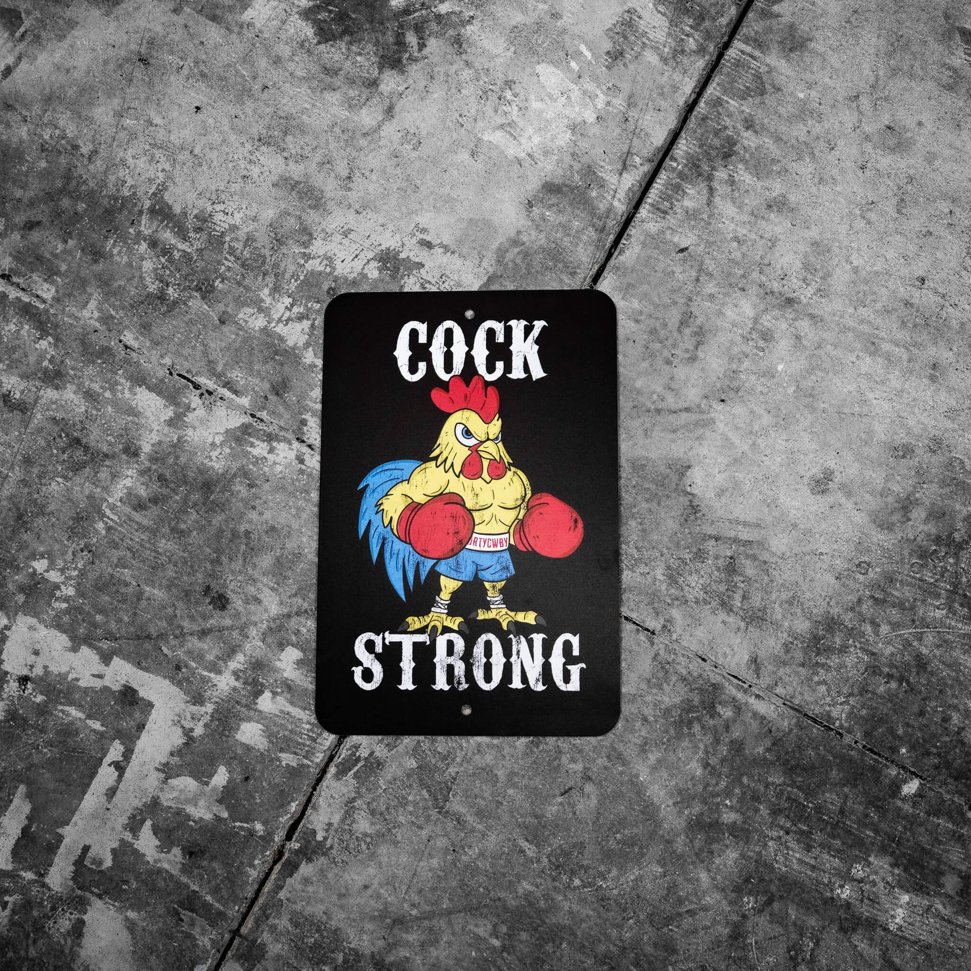 Cock Strong metal sign by Combat Iron Apparel displayed on concrete with a rustic feel, showcasing its unique design.