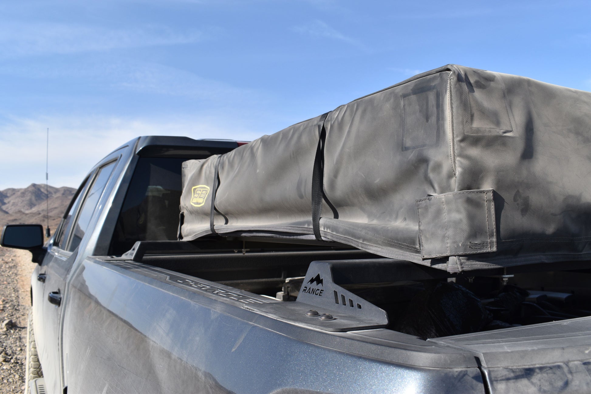 Close-up of the Range Industries 2019+ Silverado/Sierra 1500 Low Profile Tent Rack featuring a mounted tent bag, showcasing the rugged design on a pickup truck in a scenic landscape.
