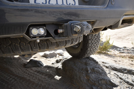 2019+ Silverado/Sierra 1500 Rear Facing Light Mount by Range Industries, showcasing Baja Designs S2 light installed near the hitch receiver on rough terrain.