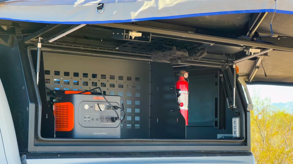 Interior view of the Dirtbox Overland Side Molle Box in a truck bed, displaying gear storage options including a generator and fire extinguisher.