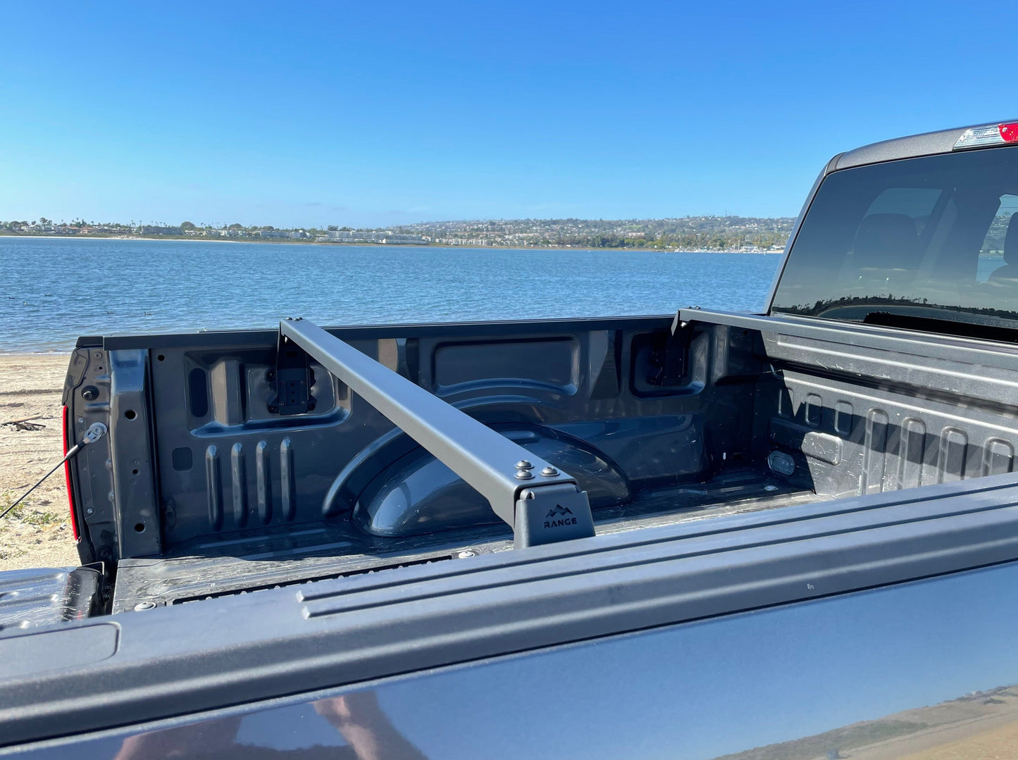 View of the Range Industries 2015+ F-150 Low Profile Rooftop Tent Rack Kit installed in a truck bed by the seaside, showcasing crossbars and factory mounting holes.