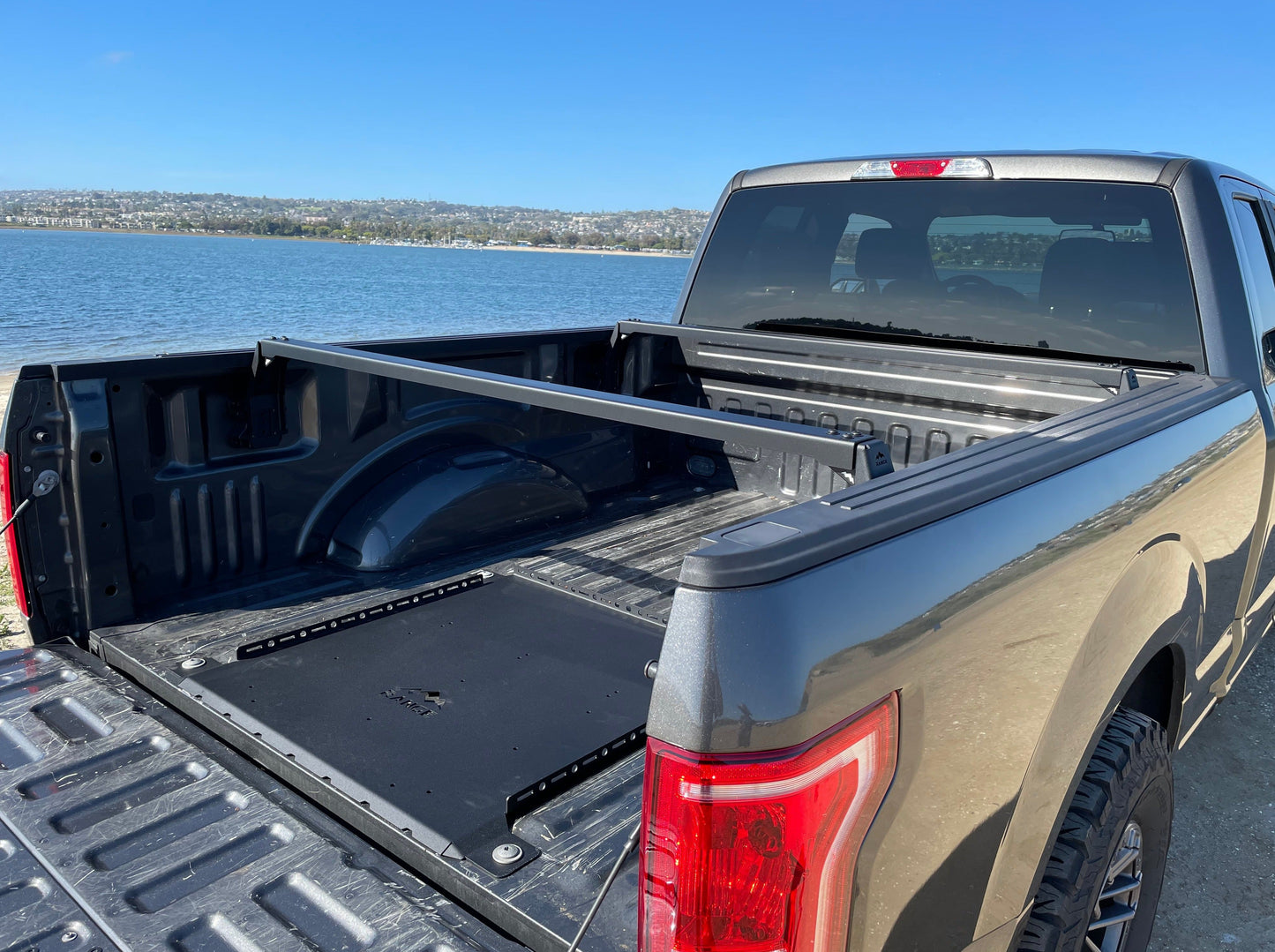2015+ F-150 Low Profile Rooftop Tent Rack Kit by Range Industries, displaying the interior of the truck bed with the tent rack system installed, overlooking a beautiful bay.