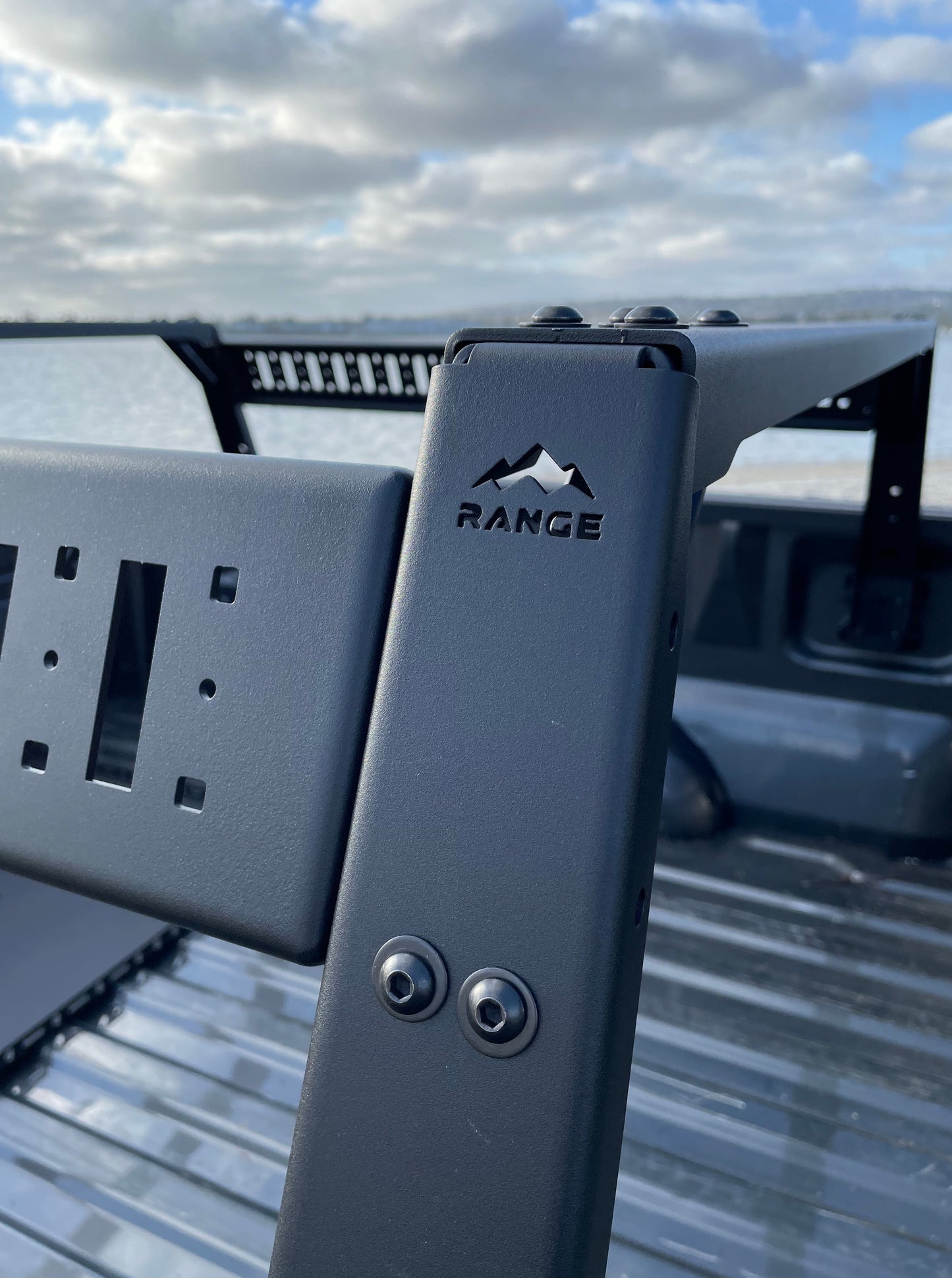 Close-up of the Range Industries F-150 Mid Height Rooftop Tent Rack Kit, showcasing the durable metal structure and box link replacement system with a scenic background.