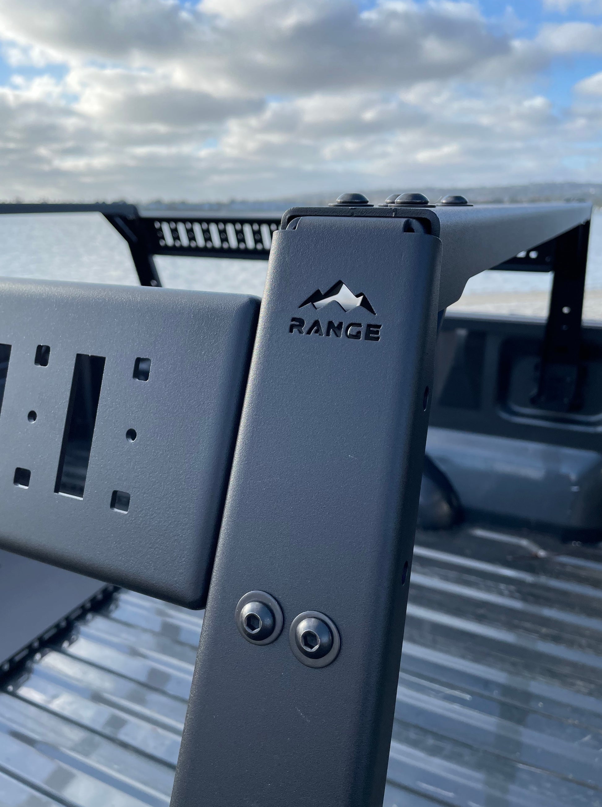 Close-up of the Range Industries F-150 Mid Height Rooftop Tent Rack Kit, showcasing the durable metal structure and box link replacement system with a scenic background.
