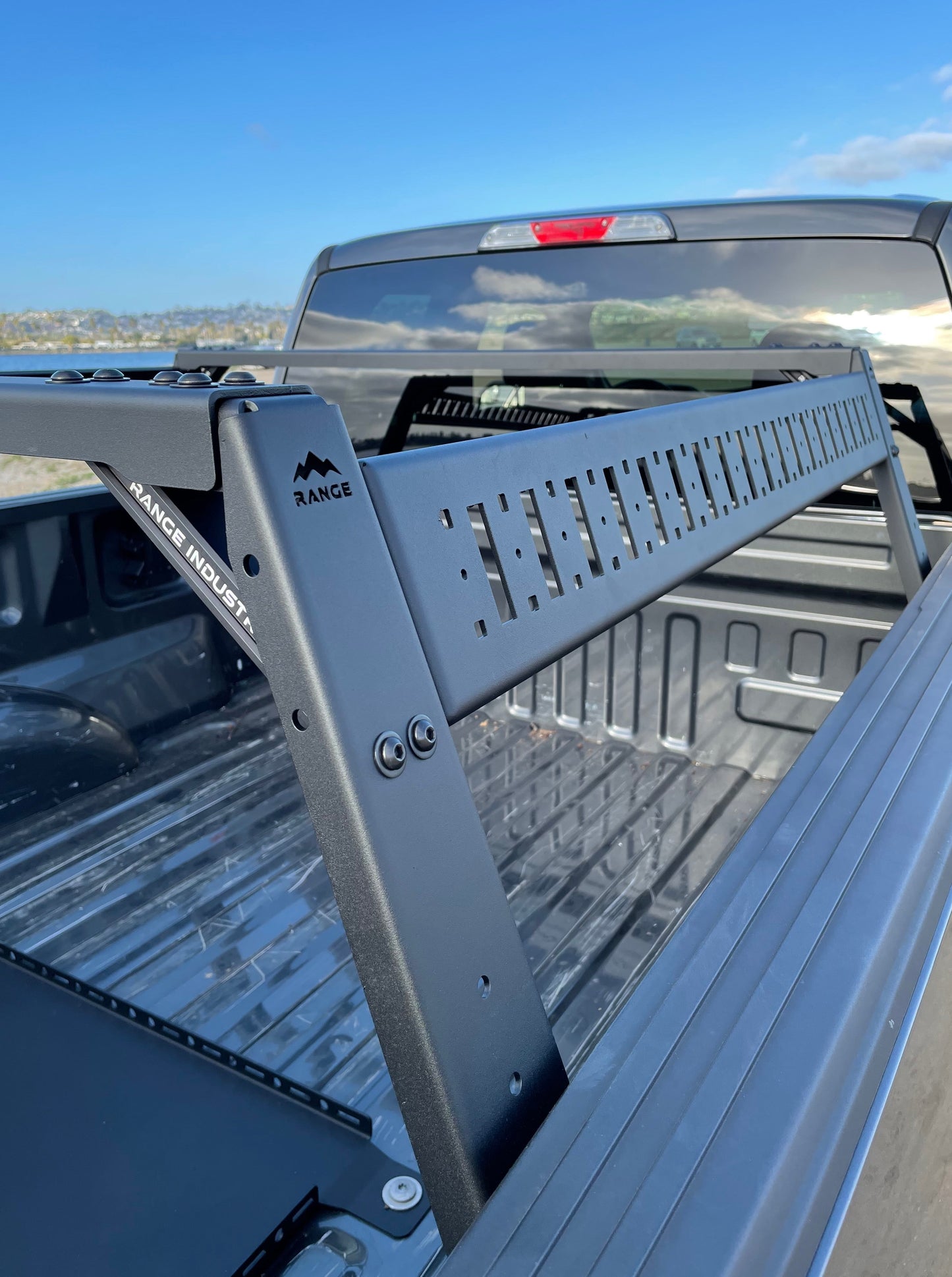View of the Range Industries F-150 Mid Height Rooftop Tent Rack Kit installed in a truck bed, highlighting the sturdy design against a clear blue sky.