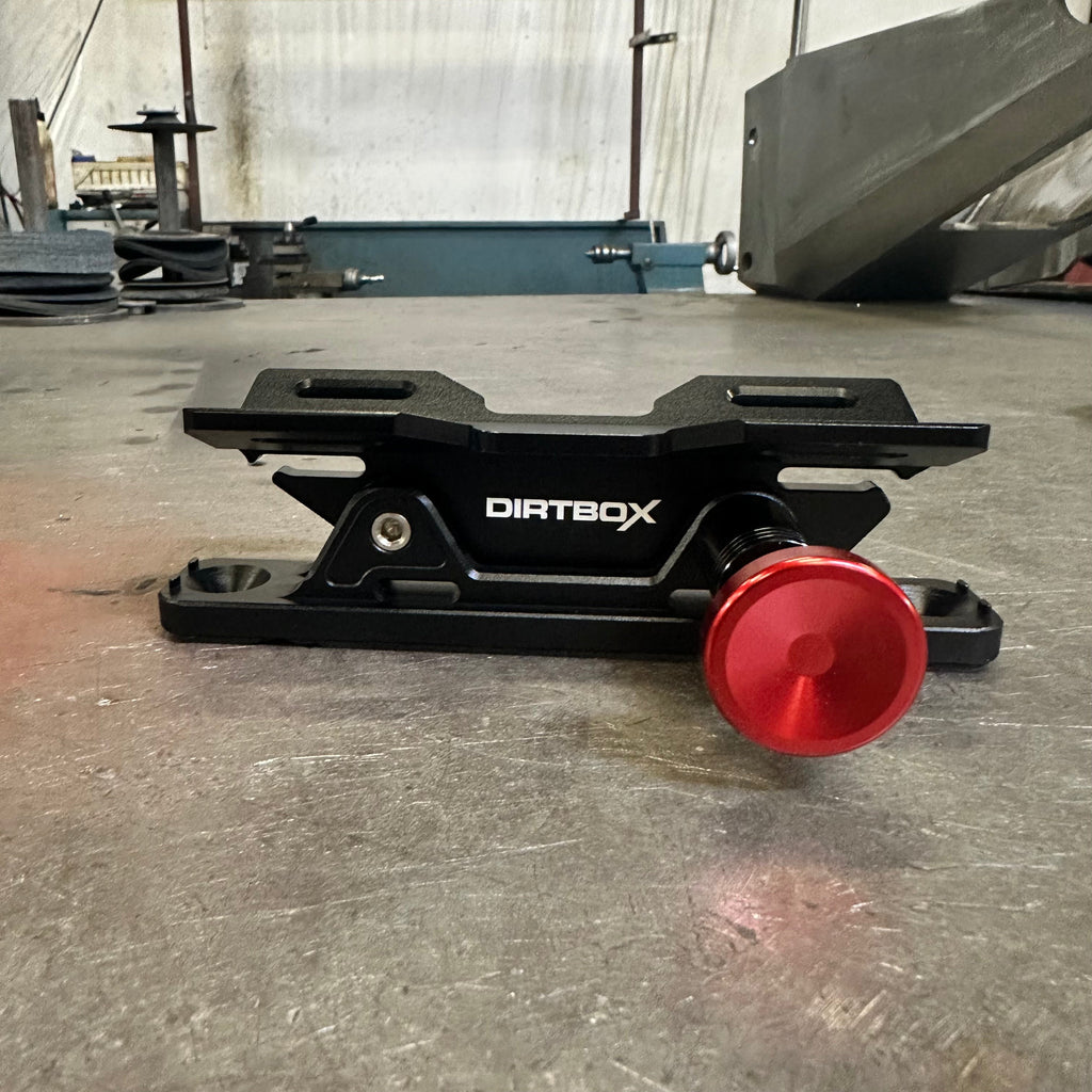 Top view of the Dirtbox Overland Quick Release Fire Extinguisher Mount, showcasing its sleek black design and red release knob on a metal surface.