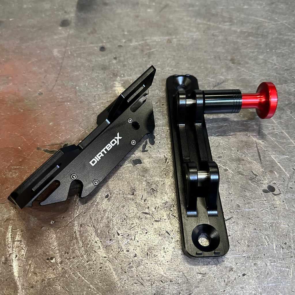 Separate parts of the Dirtbox Overland Quick Release Fire Extinguisher Mount on a metallic surface, showing the durable black components and red knob.