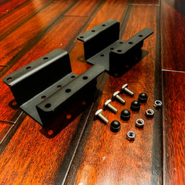 Side Hanging Water Tank Mounting Bracket by Dirtbox Overland, showcasing two black brackets with hardware on a polished wooden floor.