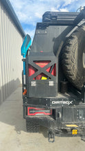 Load image into Gallery viewer, Side view of the Dirtbox Overland Jerry Can Holder attached to a vehicle, showcasing the impressive mounting options for adventure enthusiasts.