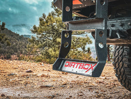 Close-up of the Dirtbox Overland Flatbed Ladder Upgrade featuring the sturdy mounting system with the brand logo, set against an outdoor rugged landscape.