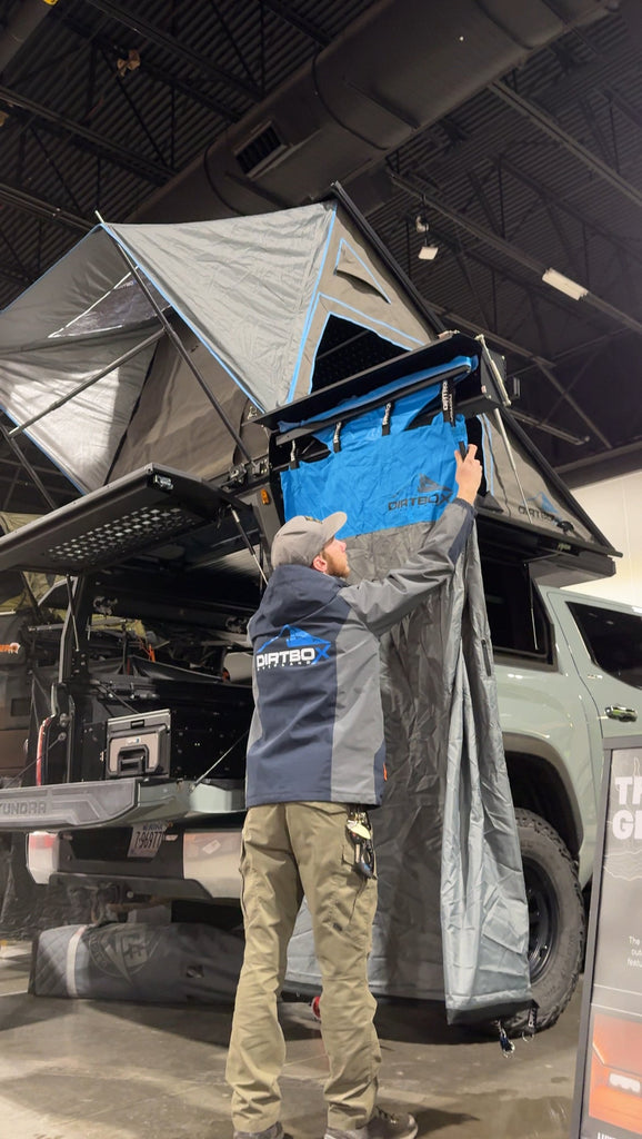 Person setting up the Ultimate Camp Shower Set by Dirtbox Overland, showcasing the hard case shower awning with a 90-degree swing out feature.