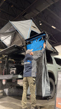 Load image into Gallery viewer, Person setting up the Ultimate Camp Shower Set by Dirtbox Overland, showcasing the hard case shower awning with a 90-degree swing out feature.