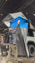 Load image into Gallery viewer, An outdoor enthusiast installing the Ultimate Camp Shower Set from Dirtbox Overland, highlighting the hard case shower and bathroom awning. The setup showcases its blue canopy against an adventure-ready vehicle.