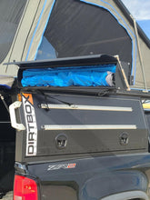 Load image into Gallery viewer, Hard case shower awning from the Ultimate Camp Shower Set by Dirtbox Overland, rolled up in the storage compartment of a truck.