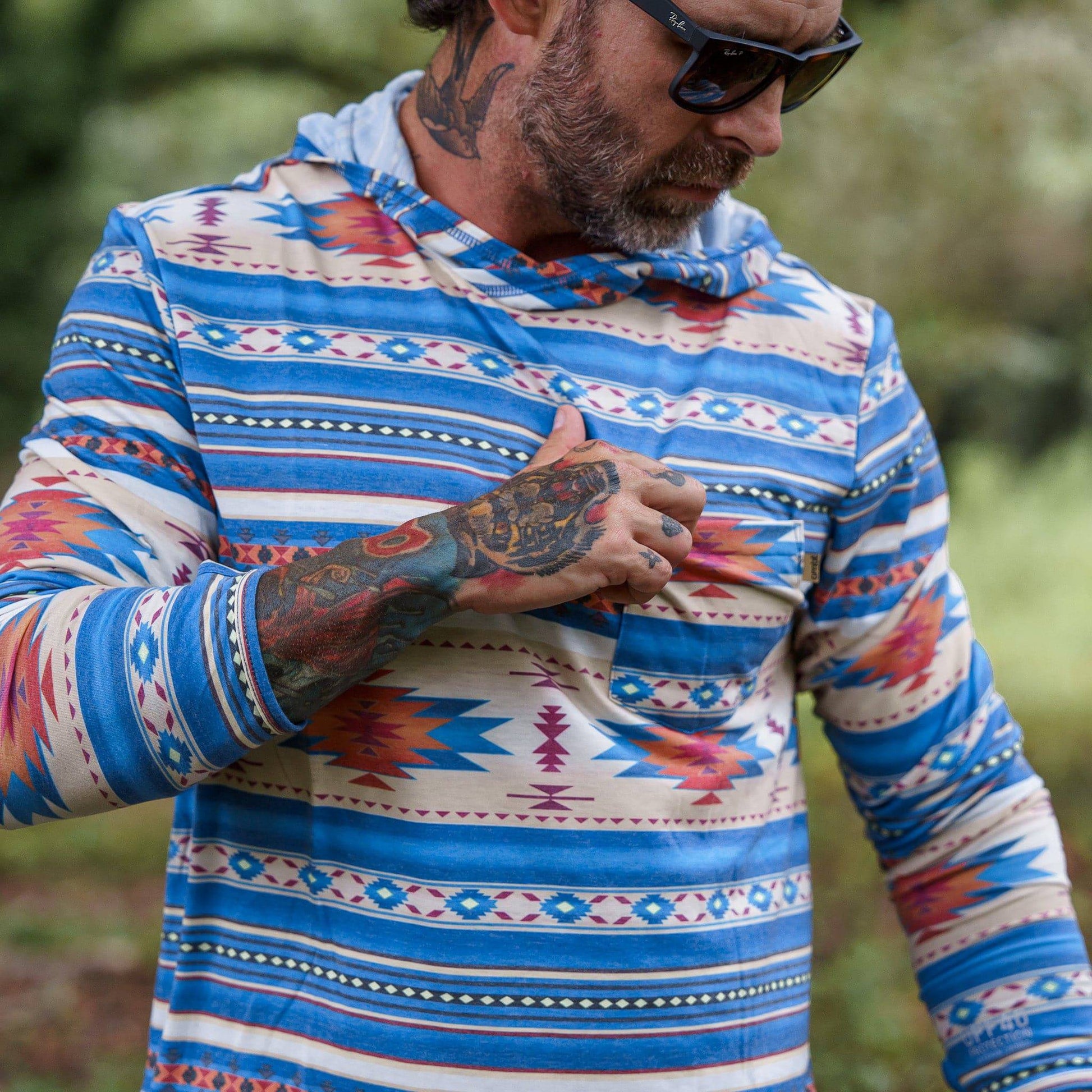 Close-up of a man wearing a Men's Outdoors Long Sleeve Performance Hoodie with tribal design by Combat Iron Apparel, highlighting the pocket detail.