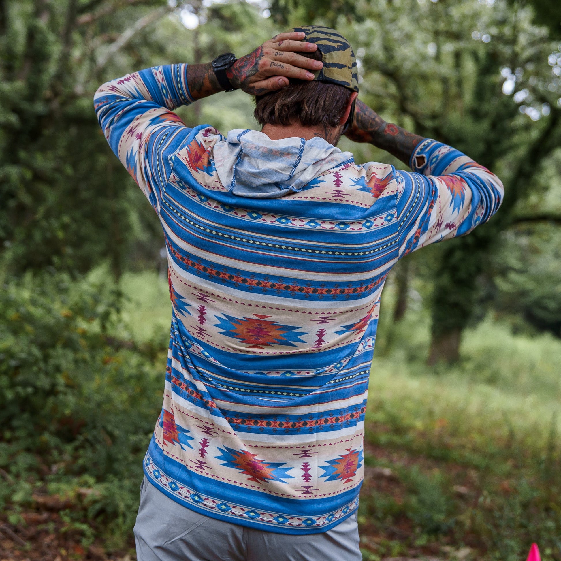 A model wearing a colorful Men's Outdoors Long Sleeve Performance Hoodie by Combat Iron Apparel, engaging in outdoor activity.