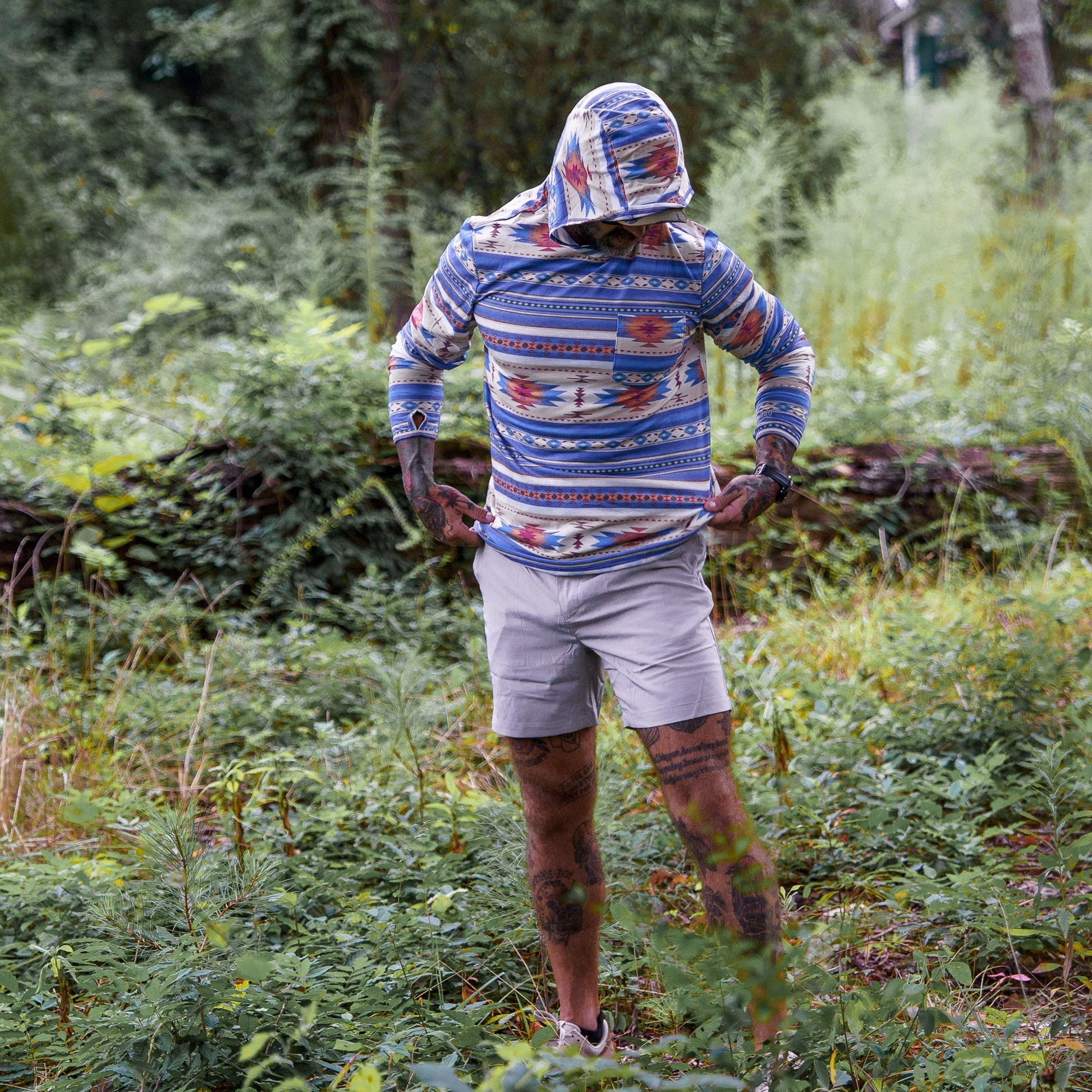 A model modeling a colorful Men's Outdoors Long Sleeve Performance Hoodie by Combat Iron Apparel in an outdoor environment.