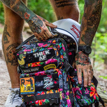 Load image into Gallery viewer, Close-up of the Combat Iron Apparel 25L Sack™ Original All-Day Molle Backpack with Pouch, featuring colorful patches on a floral background.