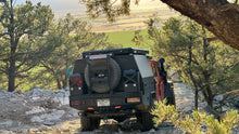 Load image into Gallery viewer, The back view of a Dirtbox Overland Flatbed System Full Box navigating a rocky path, demonstrating its functional design for outdoor exploration.