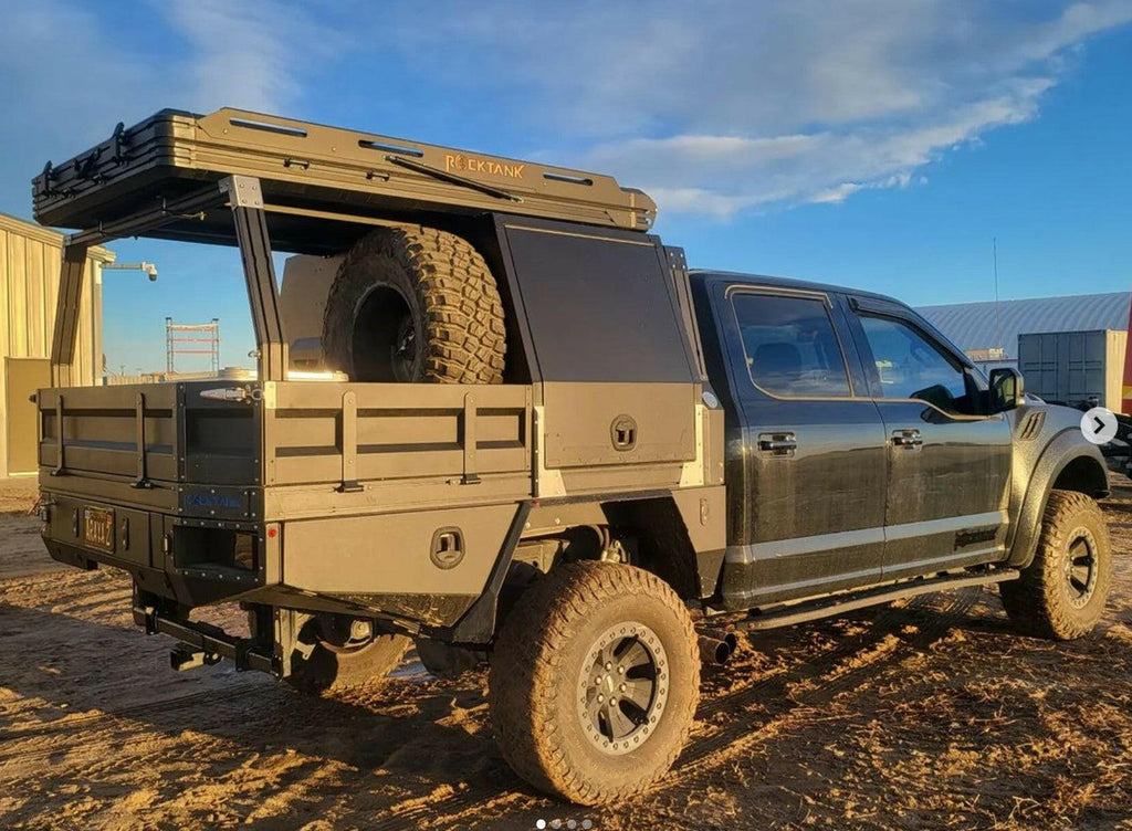 Rear angle of a truck equipped with the Dirtbox Overland Flatbed System Half Box, revealing off-road tires and spacious cargo area under a blue sky.