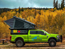 Load image into Gallery viewer, Vibrant green truck equipped with a Genesis 4‑Season Insulated Overland Camper Vehicle by Dirtbox Overland, featuring a rooftop tent, parked against a backdrop of colorful autumn trees. Perfect for rugged off-grid adventures.
