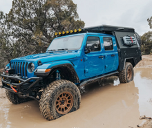 Load image into Gallery viewer, Dirtbox Overland Flatbed System Full Box on a blue Jeep in a muddy area, illustrating its durability and outdoor functionality.