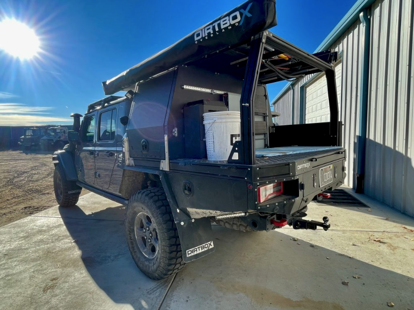 Side view of a Dirtbox Overland Flatbed System Half Box on a truck, parked in a sunny setting near storage, highlighting its functional design and practicality.