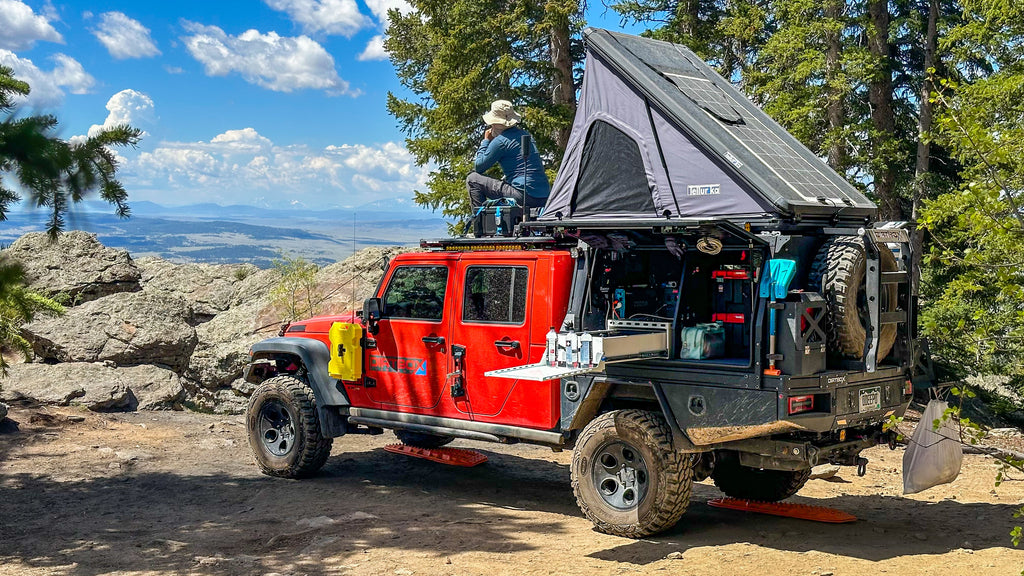 Dirtbox Overland Flatbed System Full Box on a vibrant red Jeep vehicle, parked in a picturesque mountainous setting, highlighting its outdoor cooking setup and solar panels.