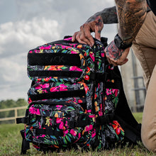 Load image into Gallery viewer, Combat Iron Apparel 25L Sack™ Original All-Day Molle Backpack with Pouch, designed with a vibrant floral pattern being handled outdoors.