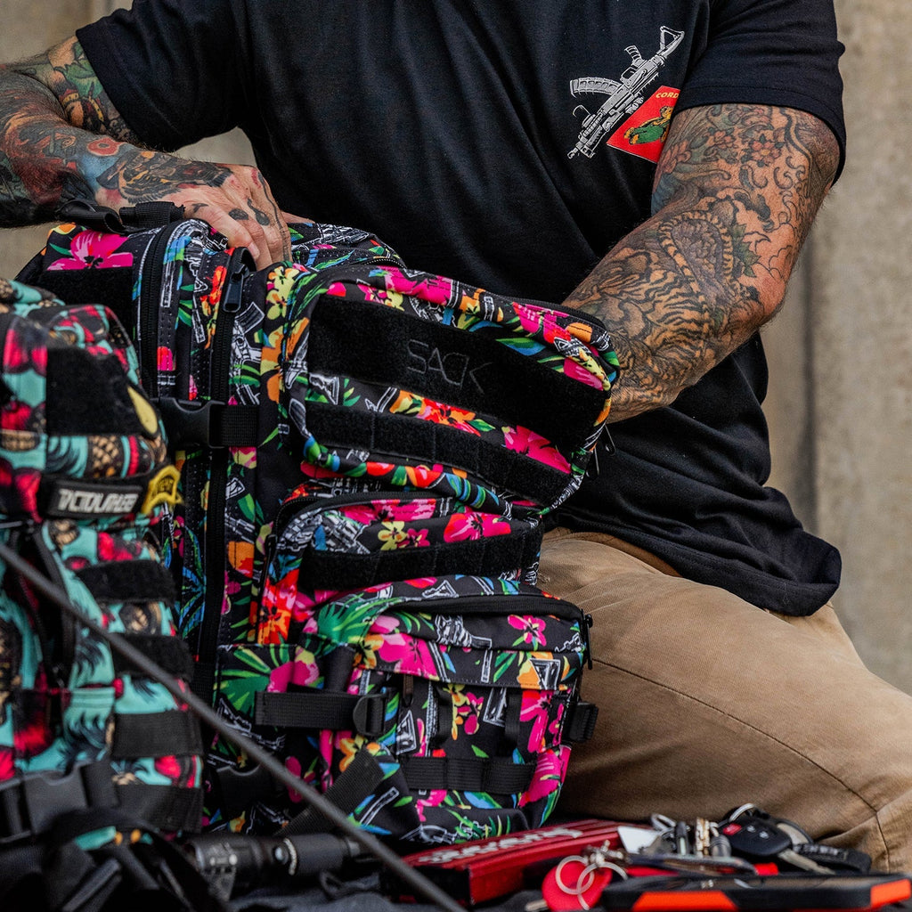Person adjusting the Combat Iron Apparel 25L Sack™ Original All-Day Molle Backpack with Pouch, surrounded by nature.