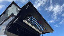 Load image into Gallery viewer, Angle view of the Security Window Molle Panel by Dirtbox Overland mounted on a canopy, displaying its customizable layout for outdoor gear.
