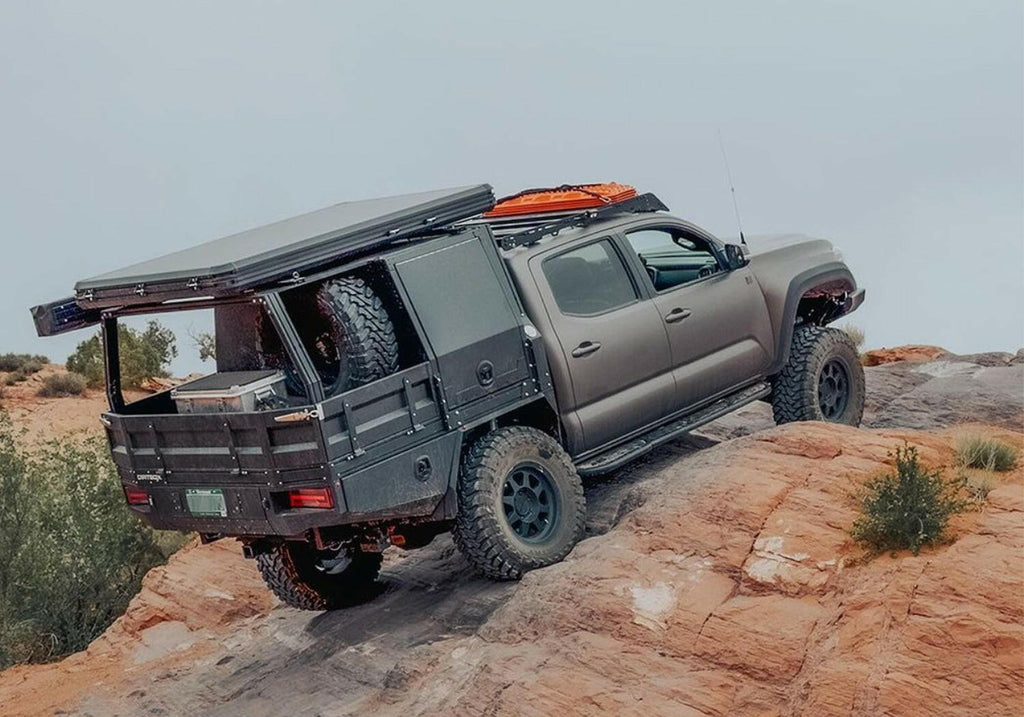 A rugged truck equipped with the Dirtbox Overland Flatbed System Half Box, showcasing its off-road capabilities on rocky terrain, perfect for adventure and utility.