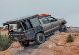A rugged truck equipped with the Dirtbox Overland Flatbed System Half Box, showcasing its off-road capabilities on rocky terrain, perfect for adventure and utility.