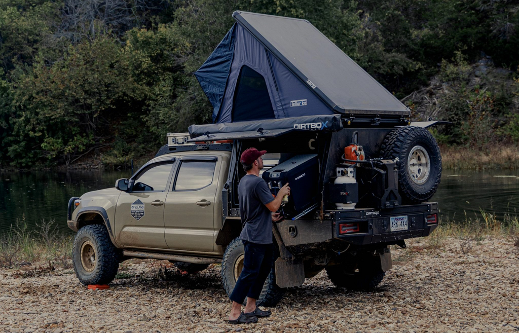 Dirtbox Overland Flatbed System Full Box installed on a truck by a river, showcasing its rugged camping features and interior lighting.