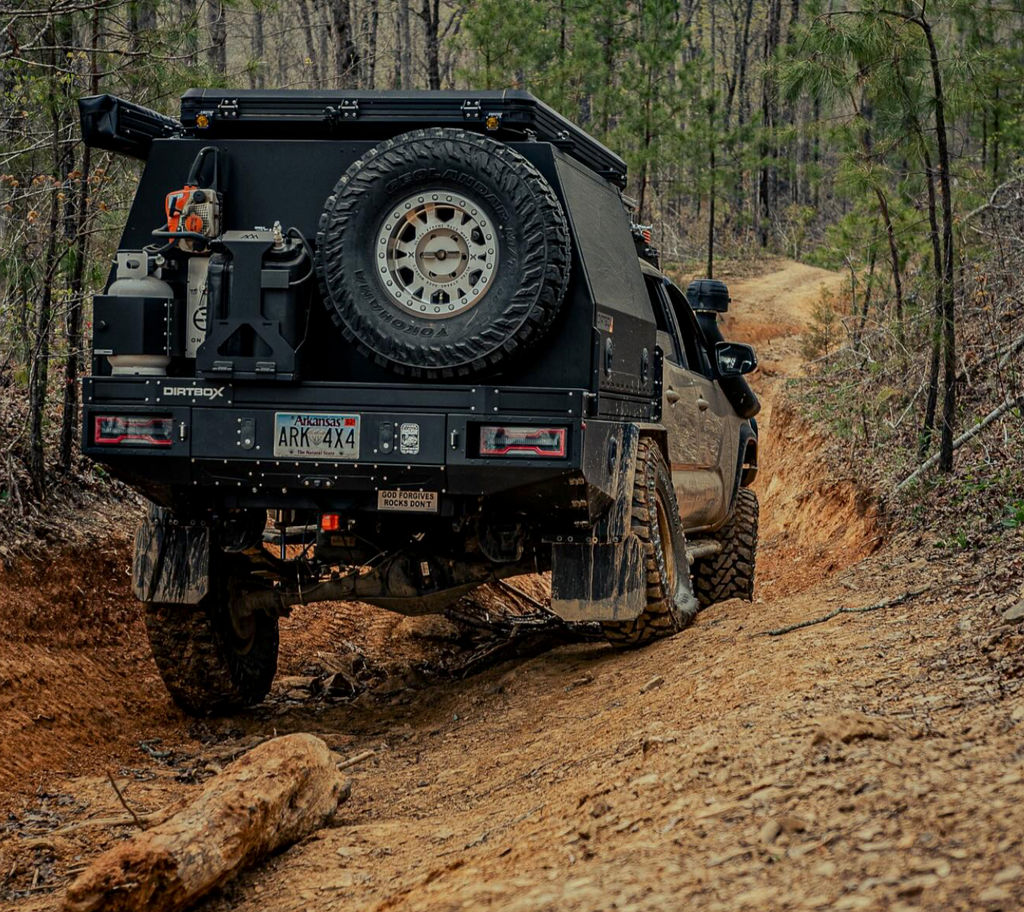 Rear view of a Dirtbox Overland Flatbed System Full Box on a truck navigating a winding dirt trail, emphasizing durability and off-road performance.