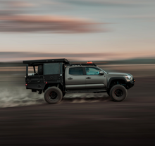 Load image into Gallery viewer, Dirtbox Overland Flatbed System Half Box mounted on a rugged truck, speeding through a dusty landscape, showcasing versatility and adventure readiness.