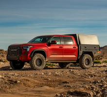 Load image into Gallery viewer, Dirtbox Overland Flatbed System Full Box mounted on a red truck parked in a desert landscape, highlighting its robust design.